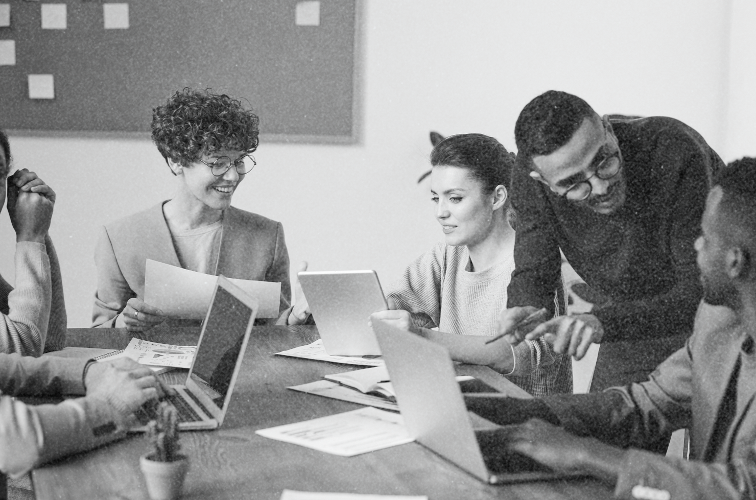 Group of diverse people in a meeting, looking at laptops and papers, discussing ideas at a table.