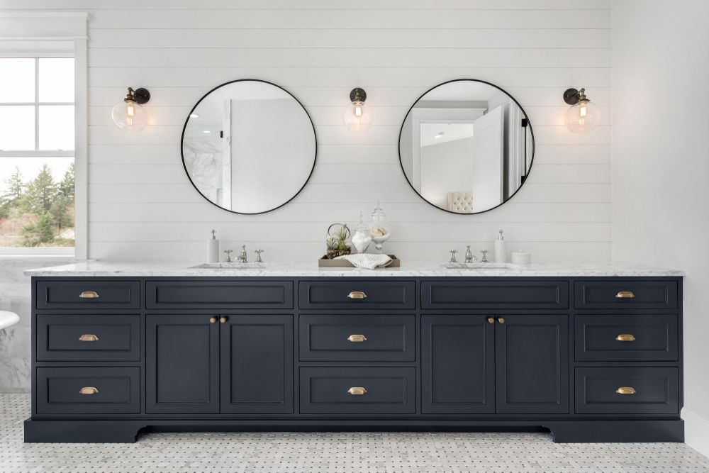 Double navy bathroom vanity with drawers, cupboards, marble benchtop and twin round mirrors on wall