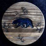 Wood round with carved bear, trees, and a dark stain.
