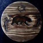 Wooden coaster with carved bear and trees.