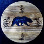 Wooden plaque with a blue bear silhouette, trees, on a textured background.