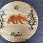 Wooden plate with a carved brown bear, trees, and branches.