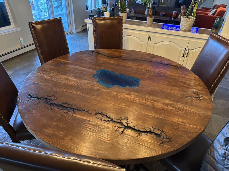 Round wooden dining table with blue epoxy inlay, surrounded by brown leather chairs.