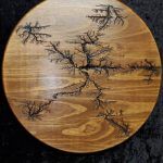 Wooden art piece with burnt Lichtenberg figure. Brown, circular, abstract pattern.
