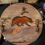 Wooden round with a bear, trees, and burnt designs.