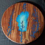 Round wooden art with blue resin lake and surrounding branches.