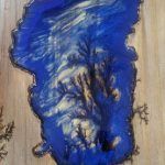 Blue resin art resembling a lake, with light-colored swirls, mounted on wood.