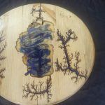 Circular wooden art with blue resin center, burnt lightning patterns, and a natural wood finish.
