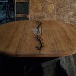 Oval wooden table with a decorative vine design in the center.