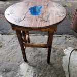 Round wooden table with blue resin inlay, set on a concrete surface.