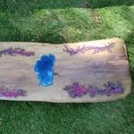 Wooden plank decorated with blue and purple floral designs, lying on grass.