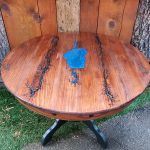 Round wooden table with dark cracks filled with black epoxy and a blue epoxy shape.