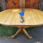 Oval wooden table with blue epoxy and black vine design, set outdoors.