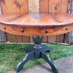 Wooden round table with dark green pedestal base, studded rim, and grassy background.