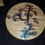 Circular wooden tabletop with colorful fractal lightning patterns in blue and purple.