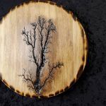 Wood-burned tree design on a circular wooden plaque with a burnt edge.