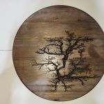 Round wooden art piece featuring a tree design burned into the wood.