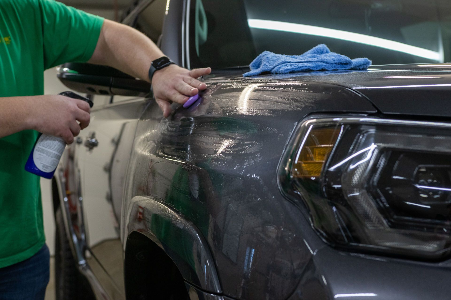 A man in a green shirt is cleaning the hood of a car.