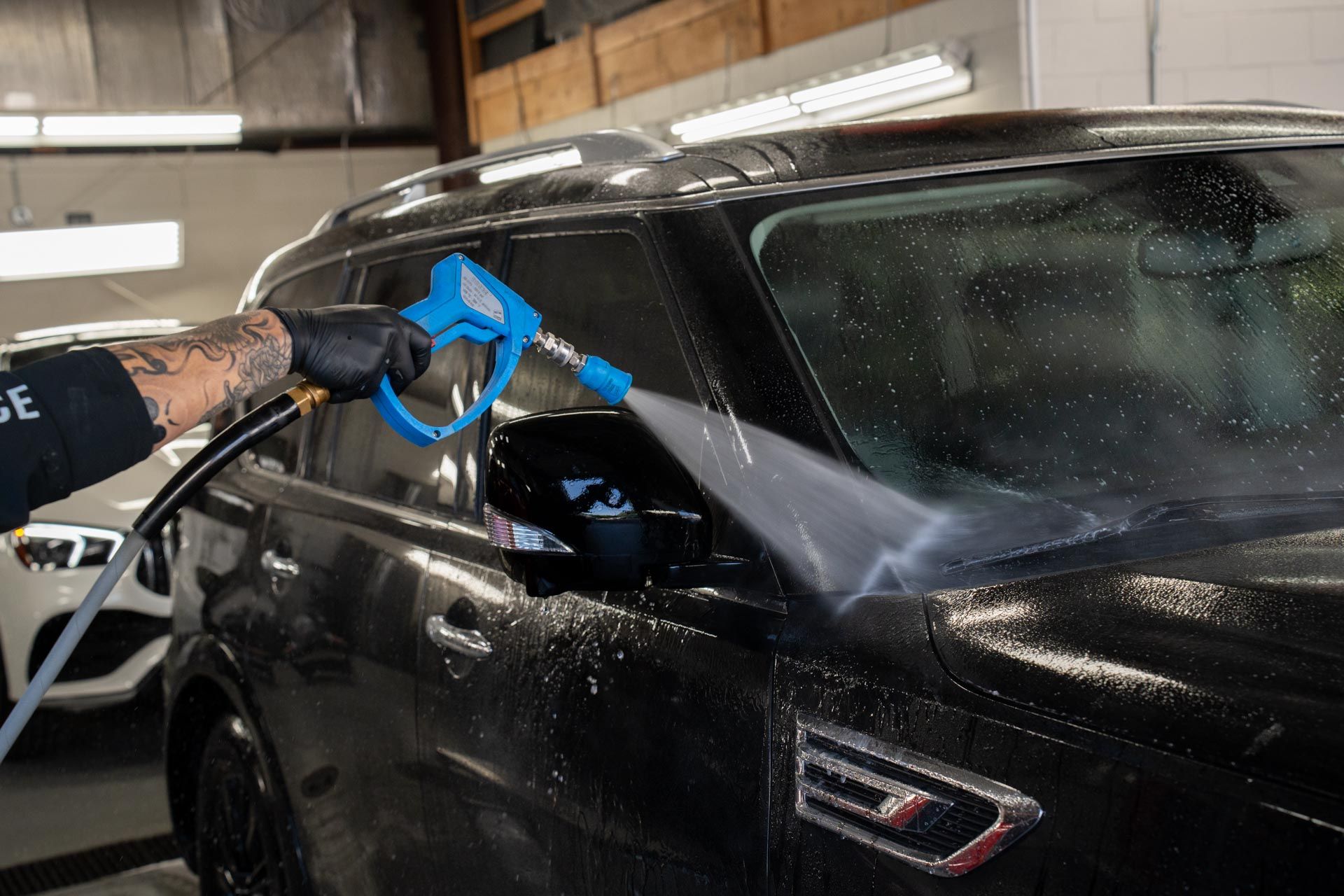 A man is washing a black car with a high pressure washer.