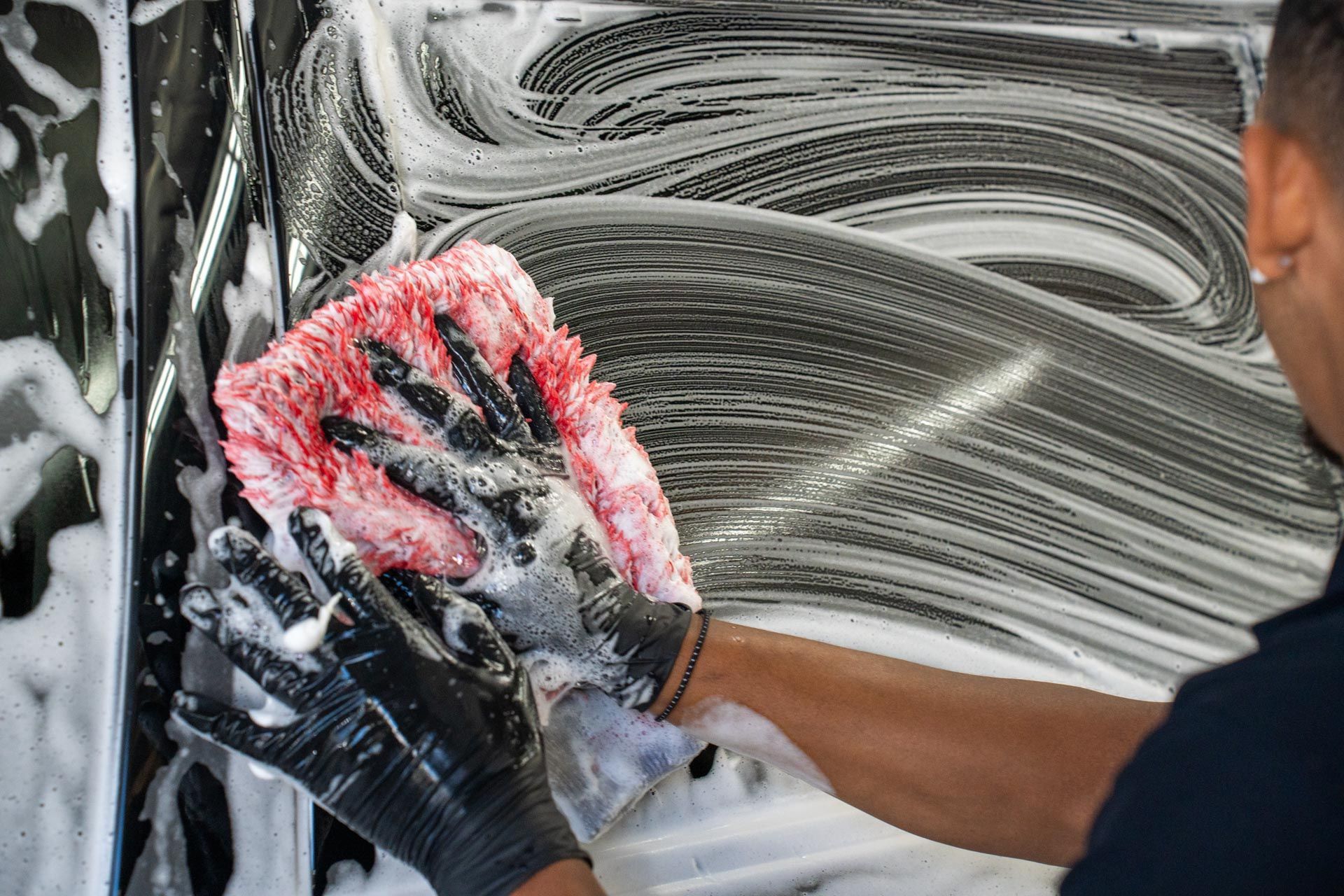 A man is washing a car with a red sponge.