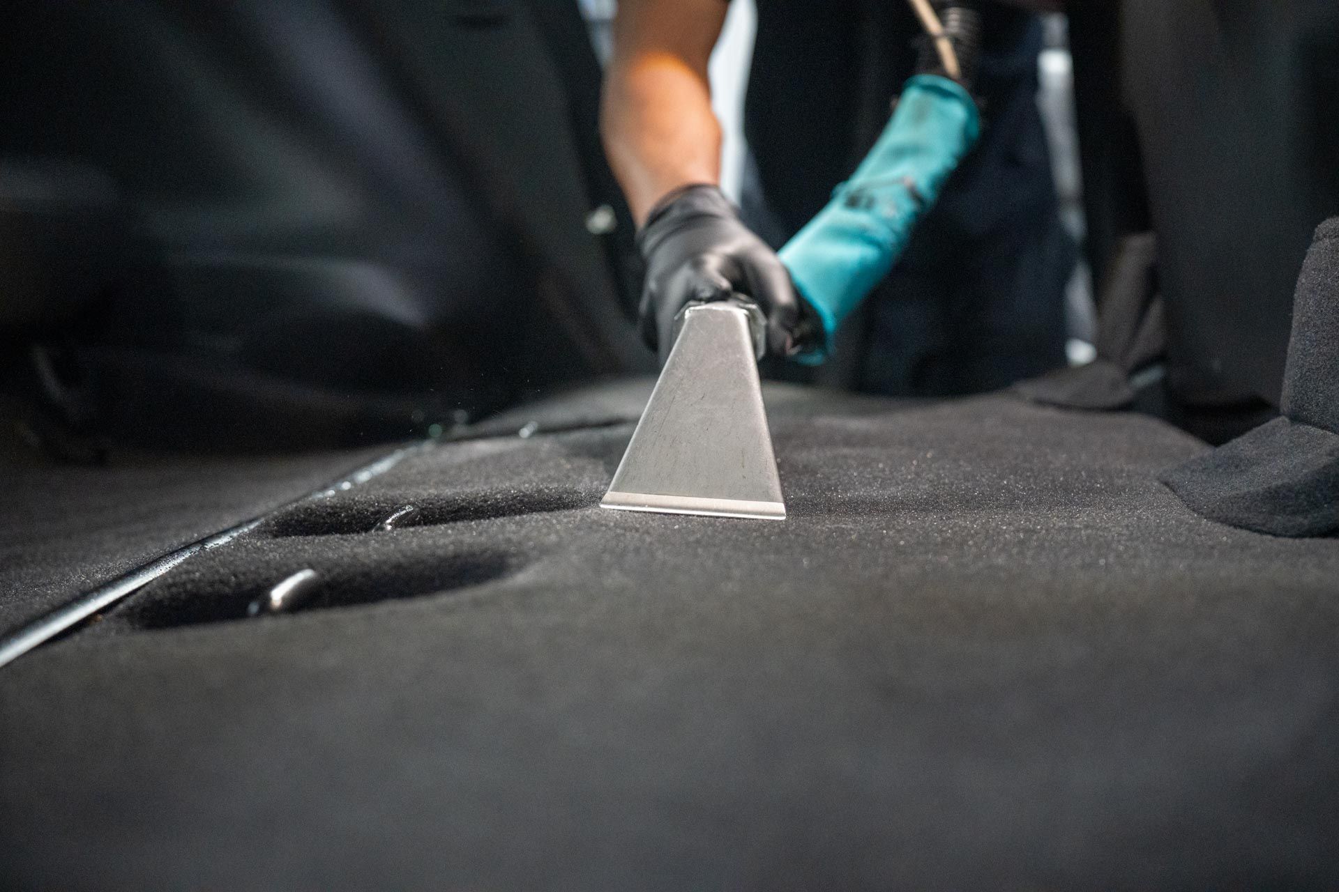 A person is cleaning the back seat of a car with a vacuum cleaner.