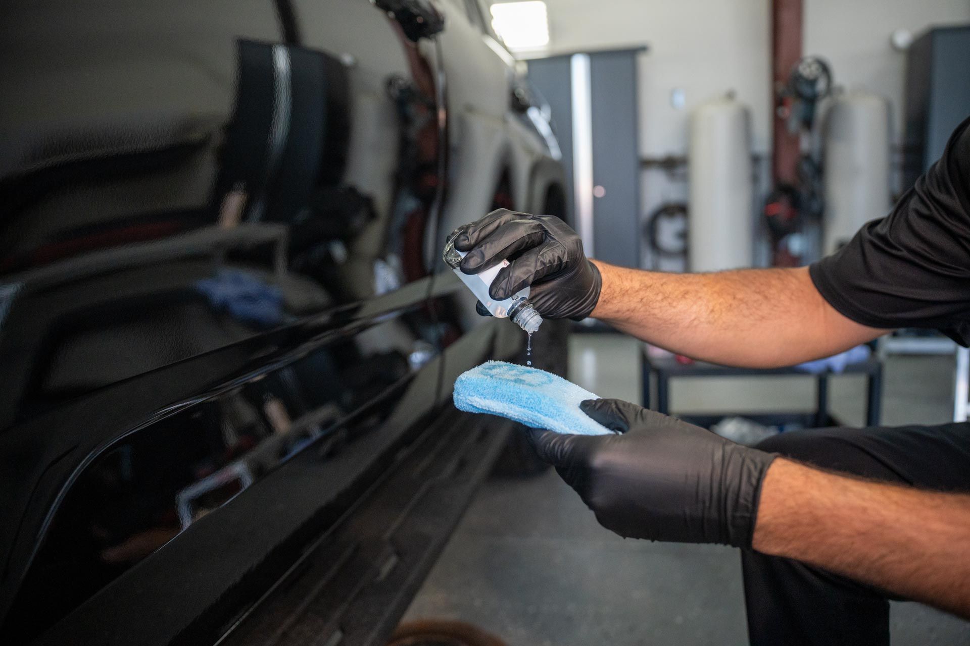 A man wearing black gloves is polishing a black car.