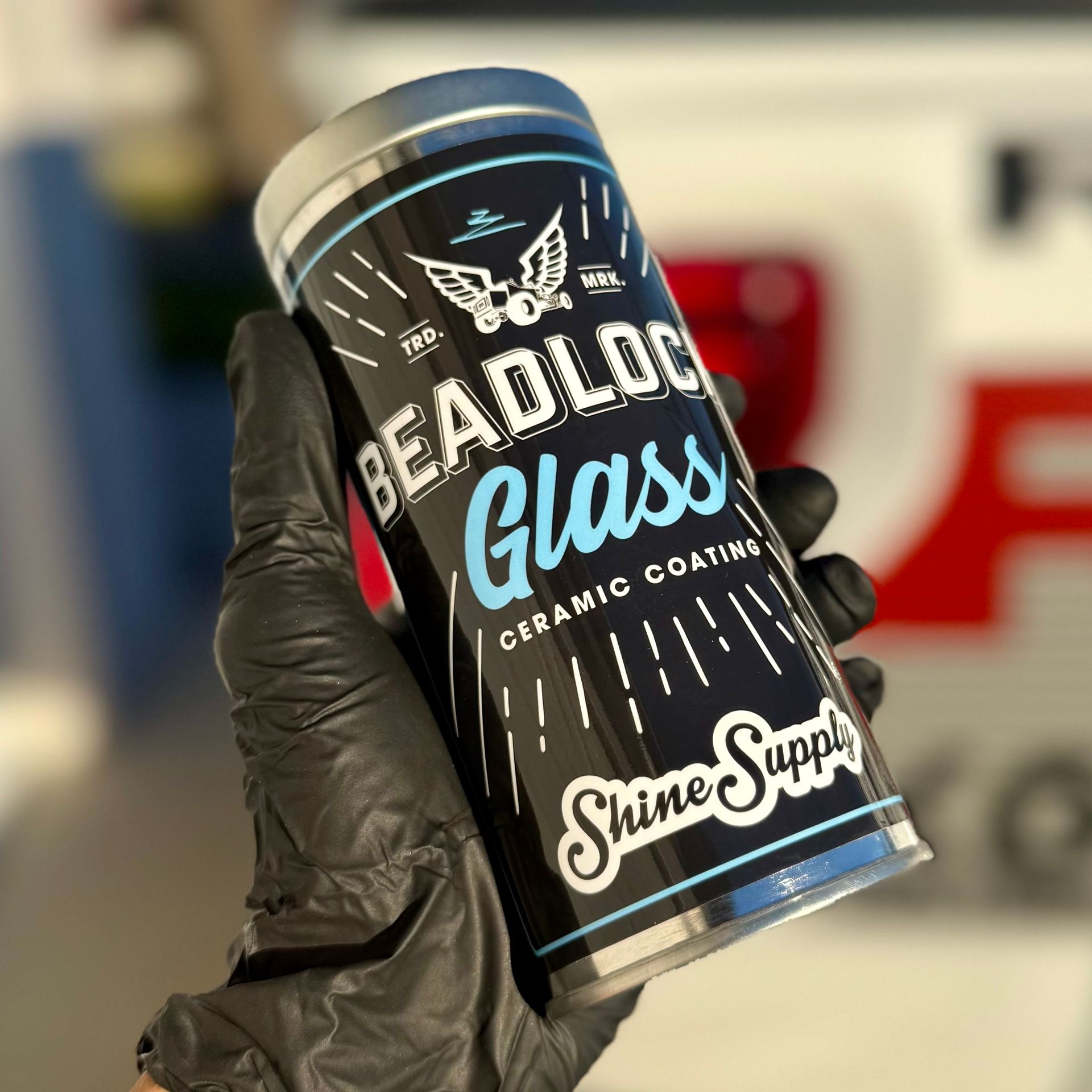 Black-gloved hand holding a cylindrical Shine Supply Beadiock Glass ceramic coating product container.