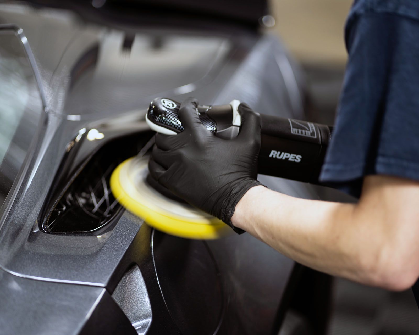 A person wearing black gloves is polishing a car with a polisher.