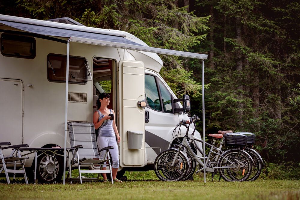 A Woman Is Standing Next To A Rv With Bikes Parked In Front Of It — Affordable Caravan Repairs in Bundaberg, QLD
