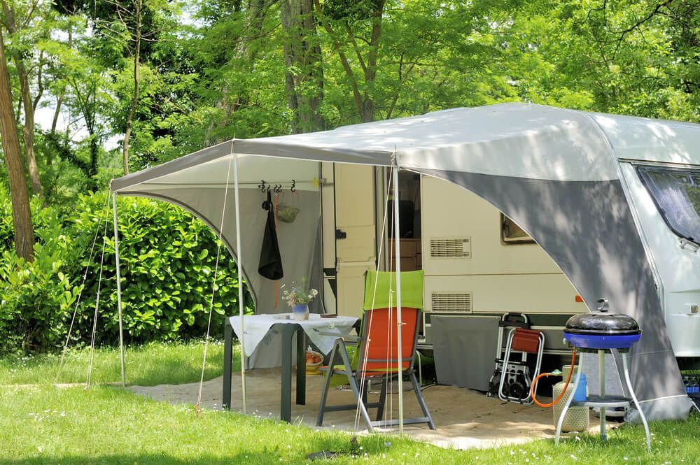 A Camper Is Parked In A Grassy Field With A Table And Chairs Under A Canopy — Affordable Caravan Repairs in Bundaberg, QLD