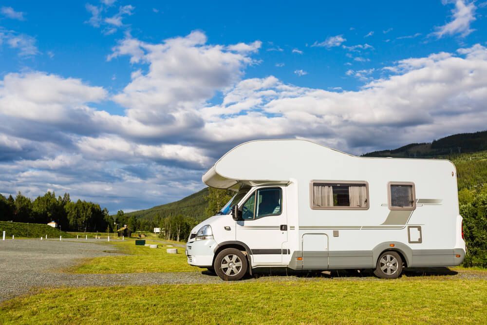 A White Rv Is Parked In A Grassy Field With Mountains In The Background — Affordable Caravan Repairs in Bundaberg, QLD