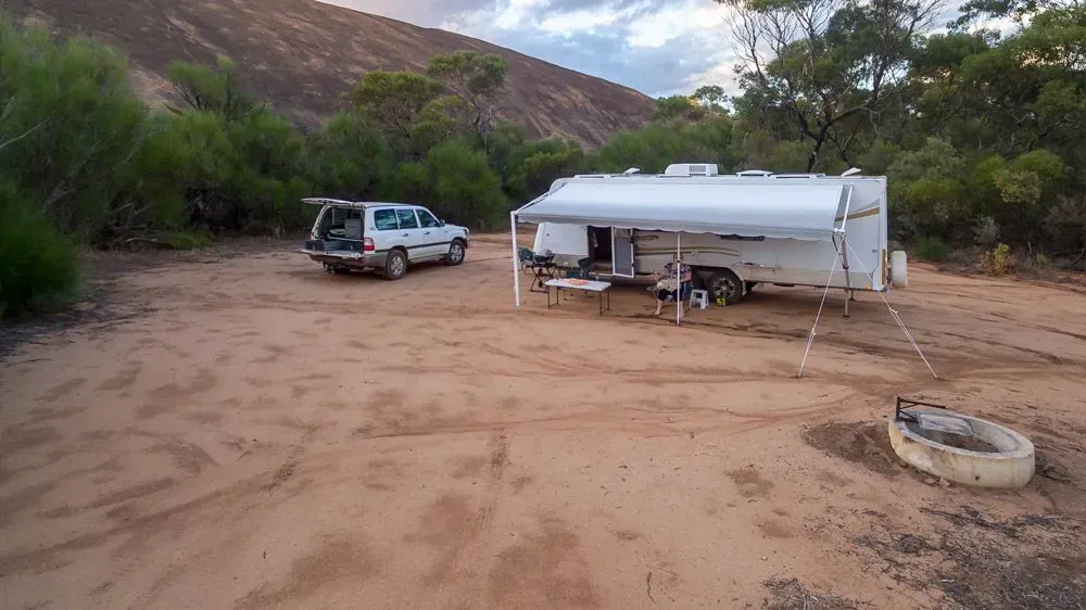 A White Caravan Is Parked Next To A Trailer In A Dirt Field — Affordable Caravan Repairs in Bundaberg, QLD