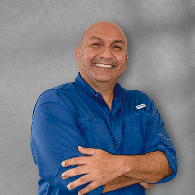 A man in a blue shirt is smiling with his arms crossed
