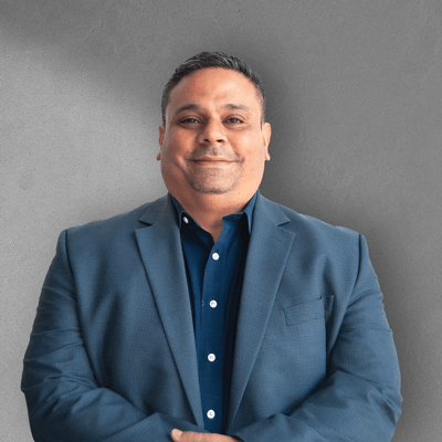 A man in a blue suit and blue shirt is standing with his arms crossed.
