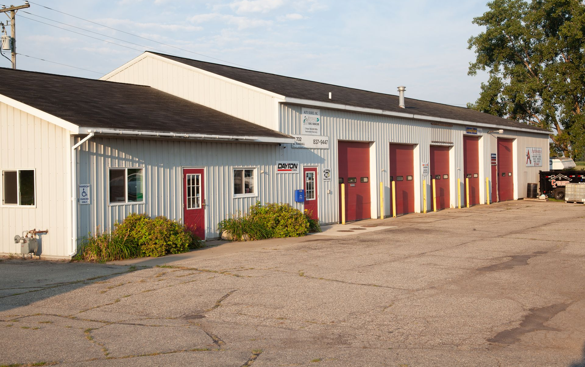 A gray metal building with several red garage doors, a banner, and a black truck parked in front. | Auto Source Of West Michigan