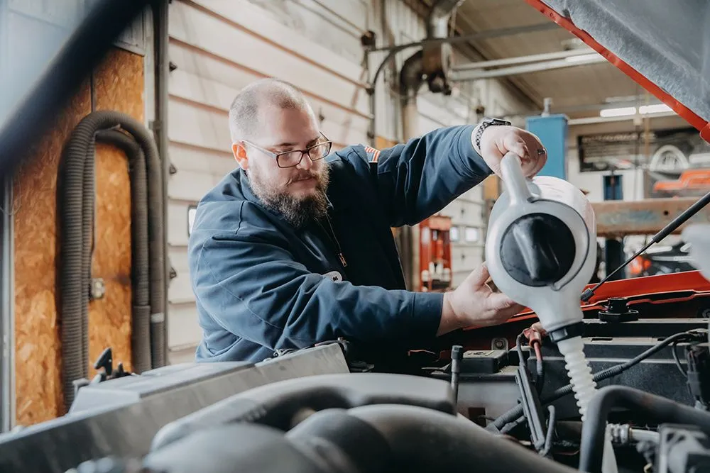 Mechanic pouring oil into a car engine in a garage. | Auto Source Of West Michigan