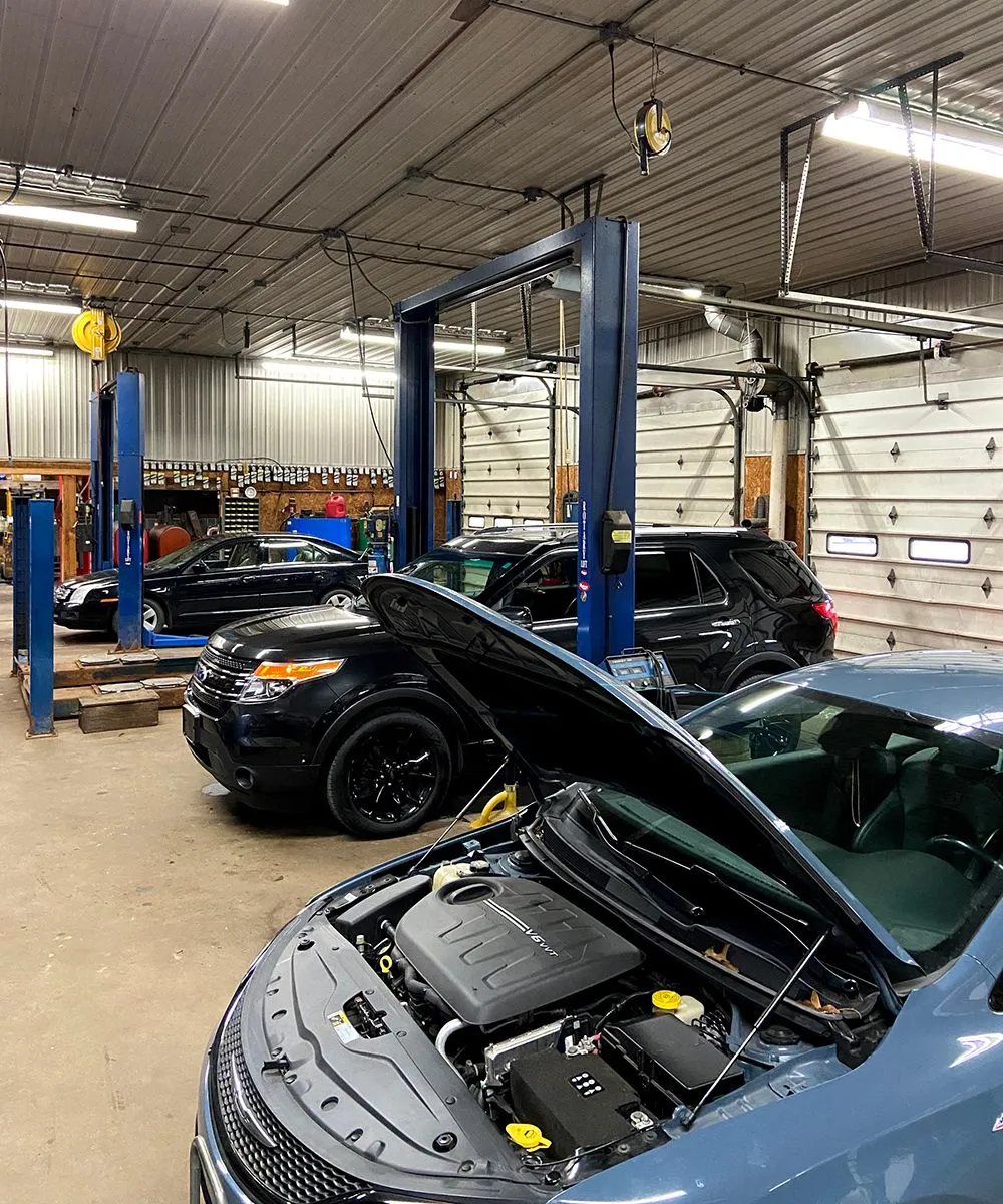 Cars in a mechanic's shop, hoods up, on lifts. Blue car in foreground; black SUVs in the background. | Auto Source Of West Michigan
