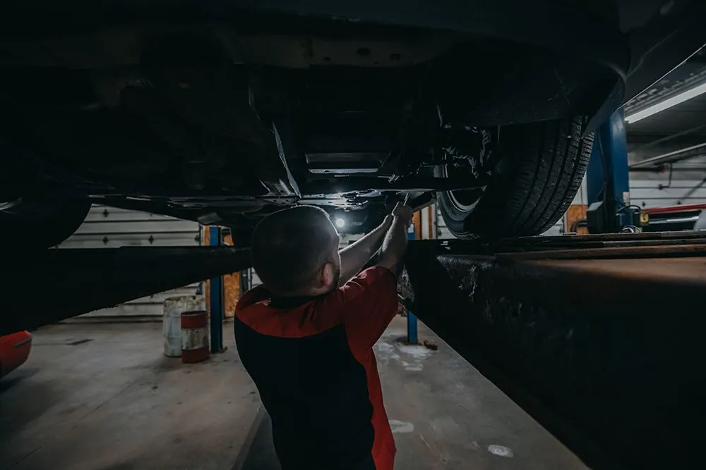 Mechanic working under a car raised on a lift in a garage. | Auto Source Of West Michigan