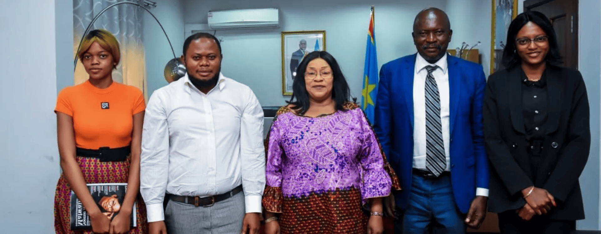 Cinq personnes posent pour une photo dans un bureau. Elles sourient et portent des tenues formelles.