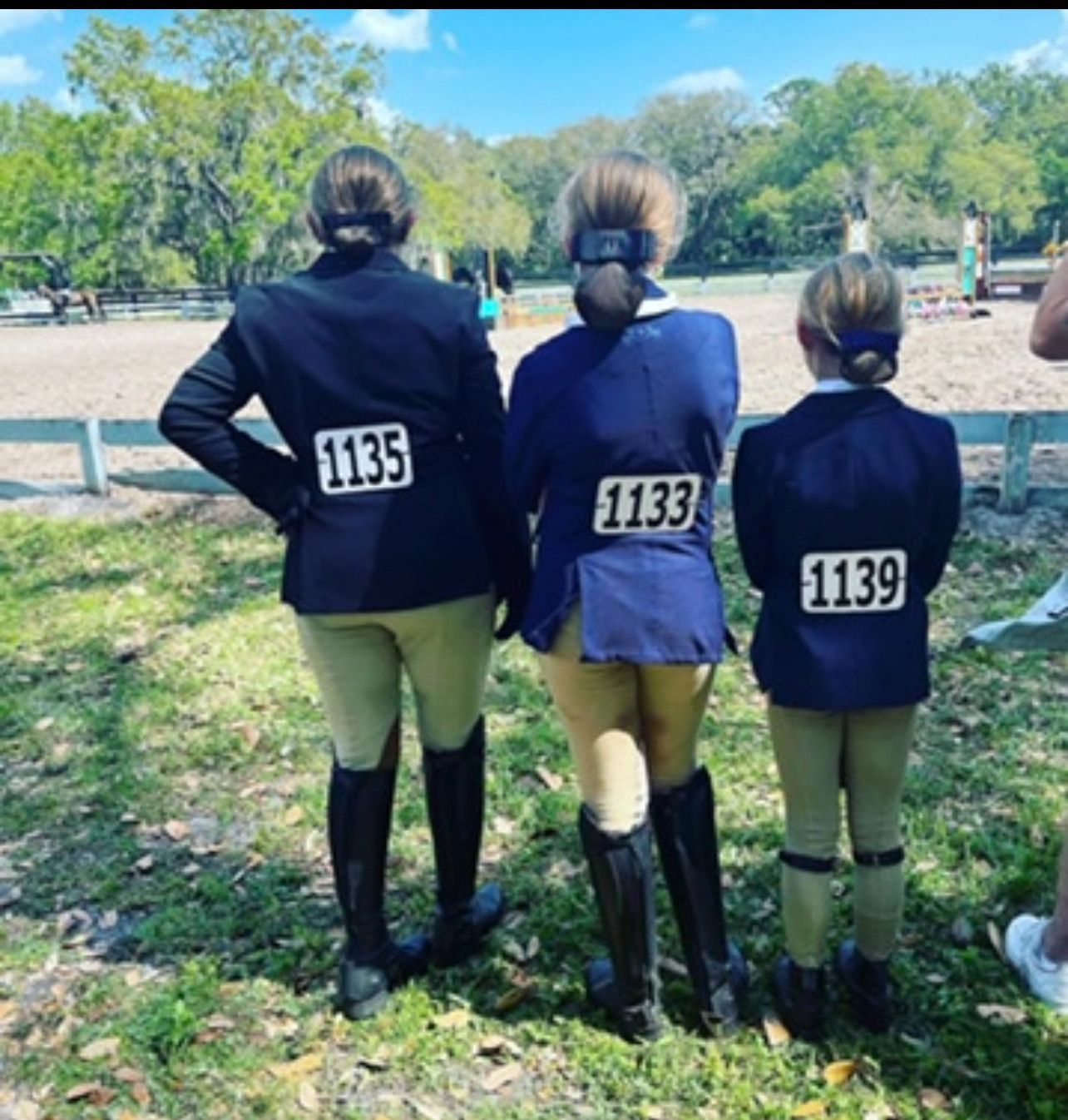 Three girls are standing in the grass with numbers on their backs
