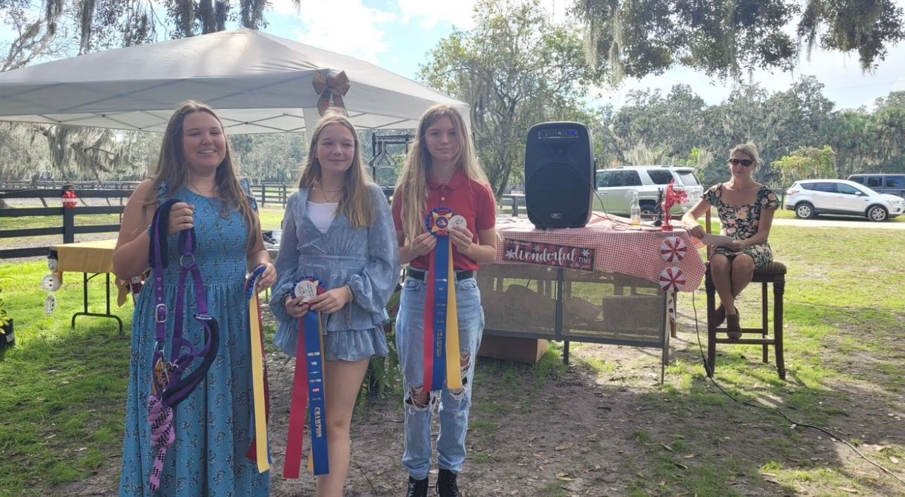 A group of young women are standing in a field holding ribbons.