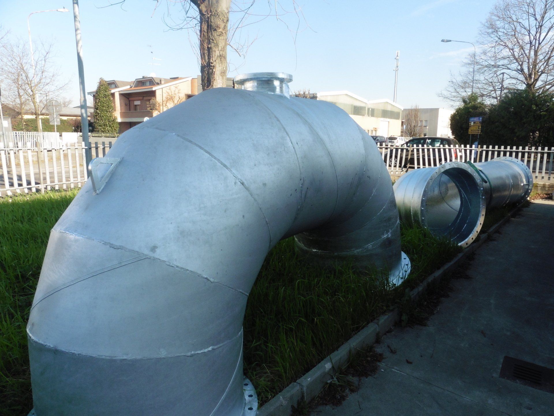 Un grande tubo di metallo è appoggiato sull'erba accanto a una recinzione
