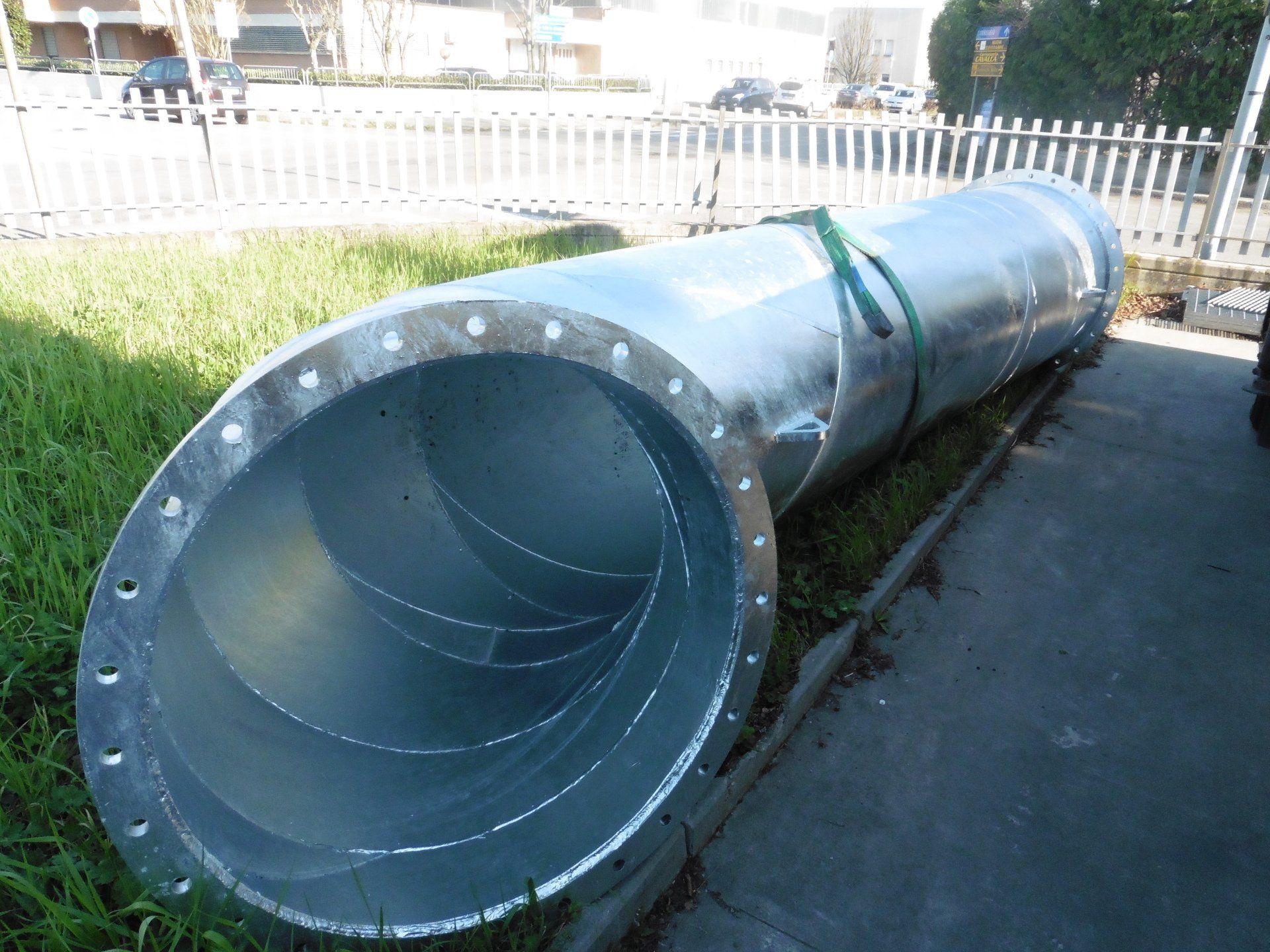 Un grande tubo di metallo è appoggiato sull'erba accanto a una recinzione.