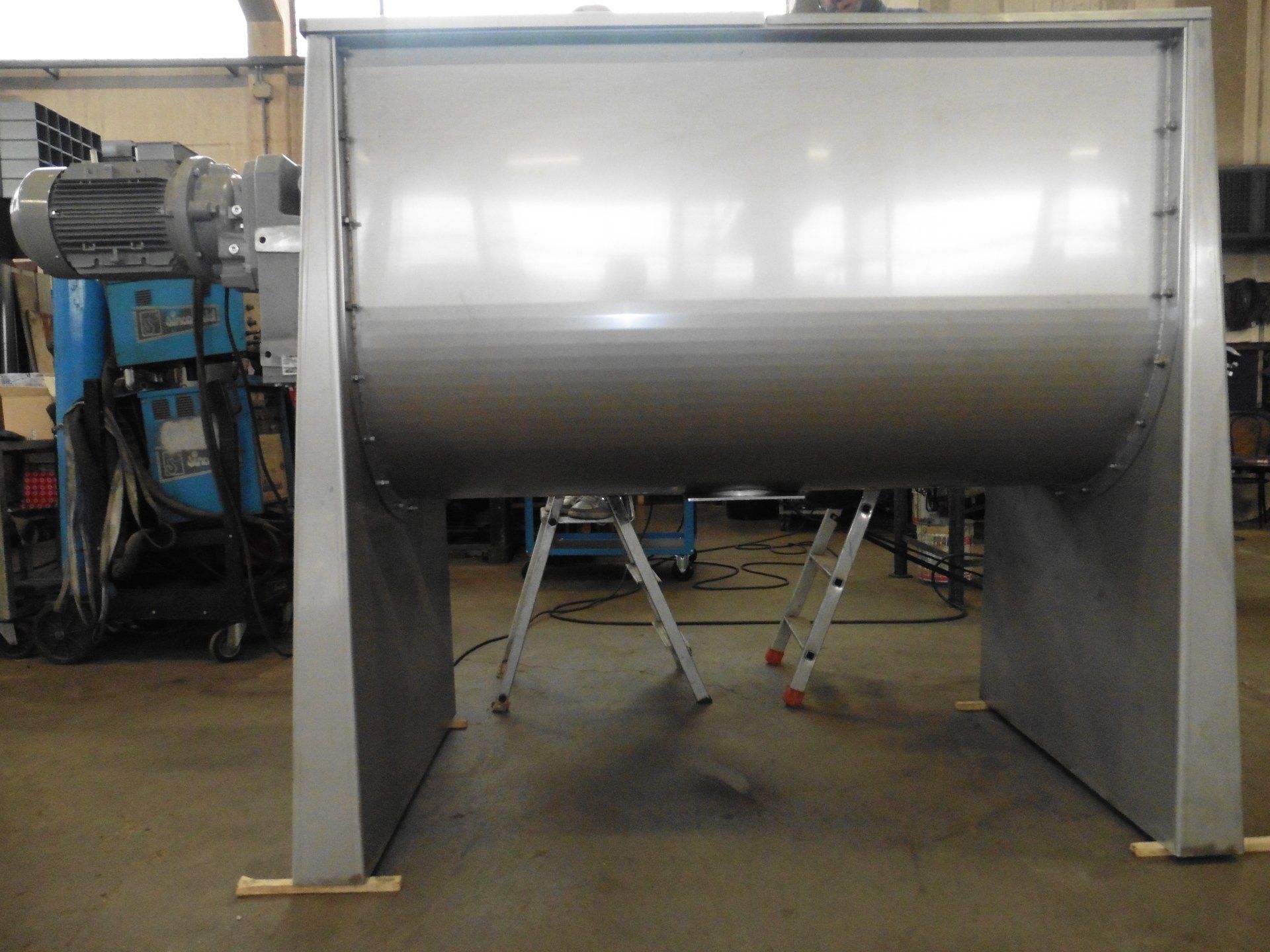 Un grande miscelatore in acciaio inossidabile è appoggiato su un supporto di legno in una fabbrica.