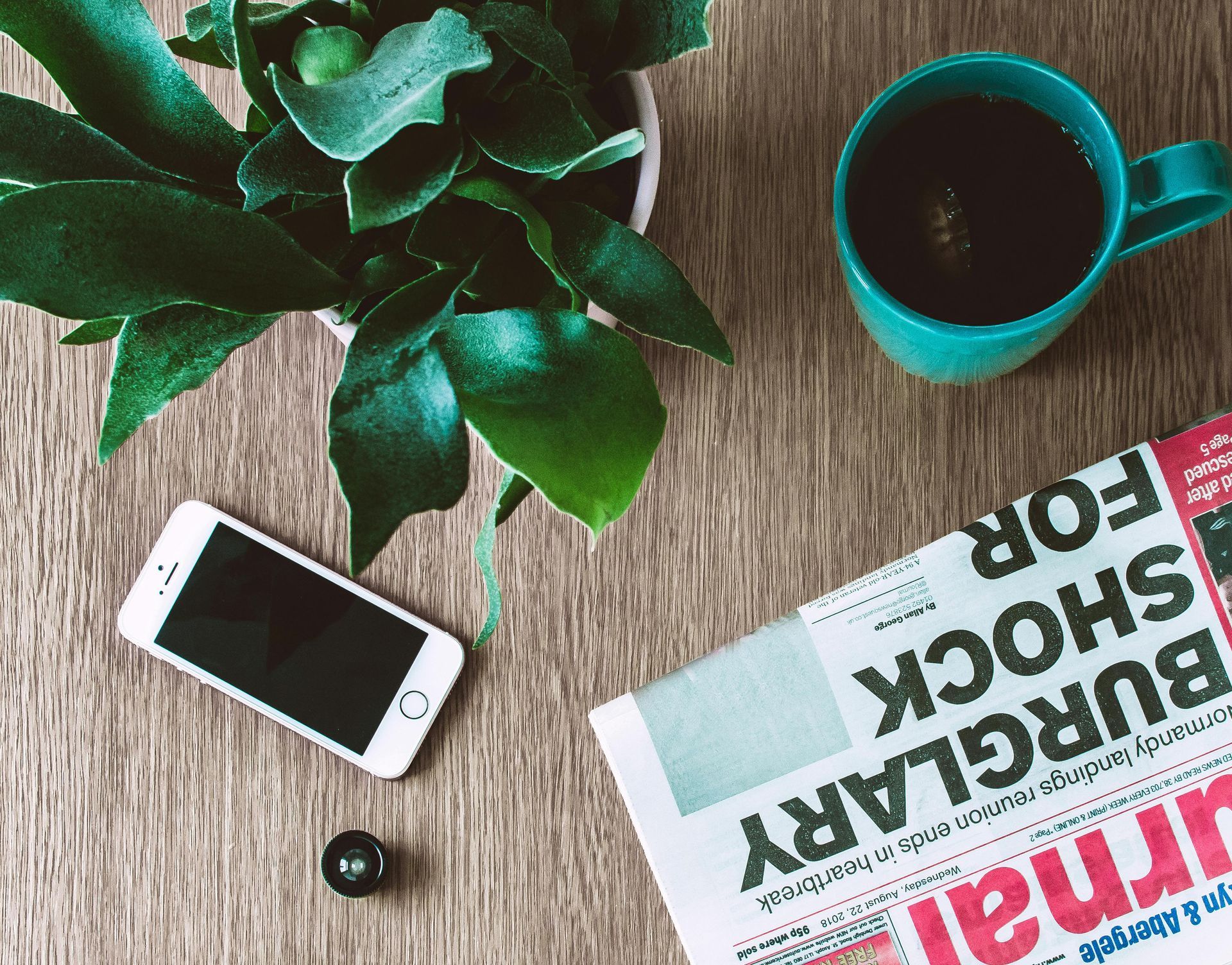Smartphone, koffiemok, plant en krant op een houten tafel.