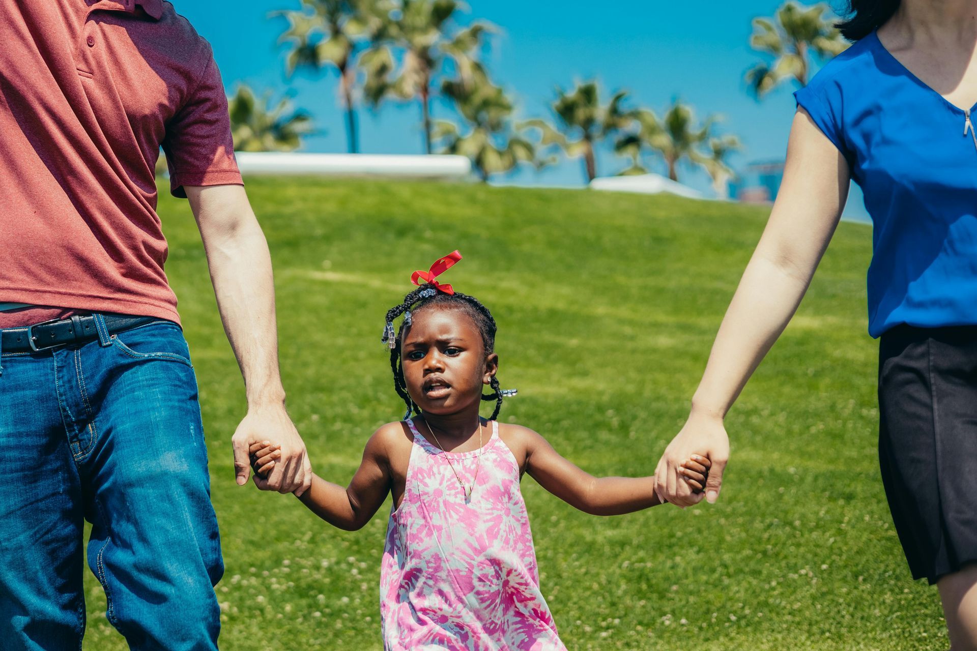 Ouders lopen hand in hand met een zwart meisje op een met gras begroeide heuvel onder de palmbomen.