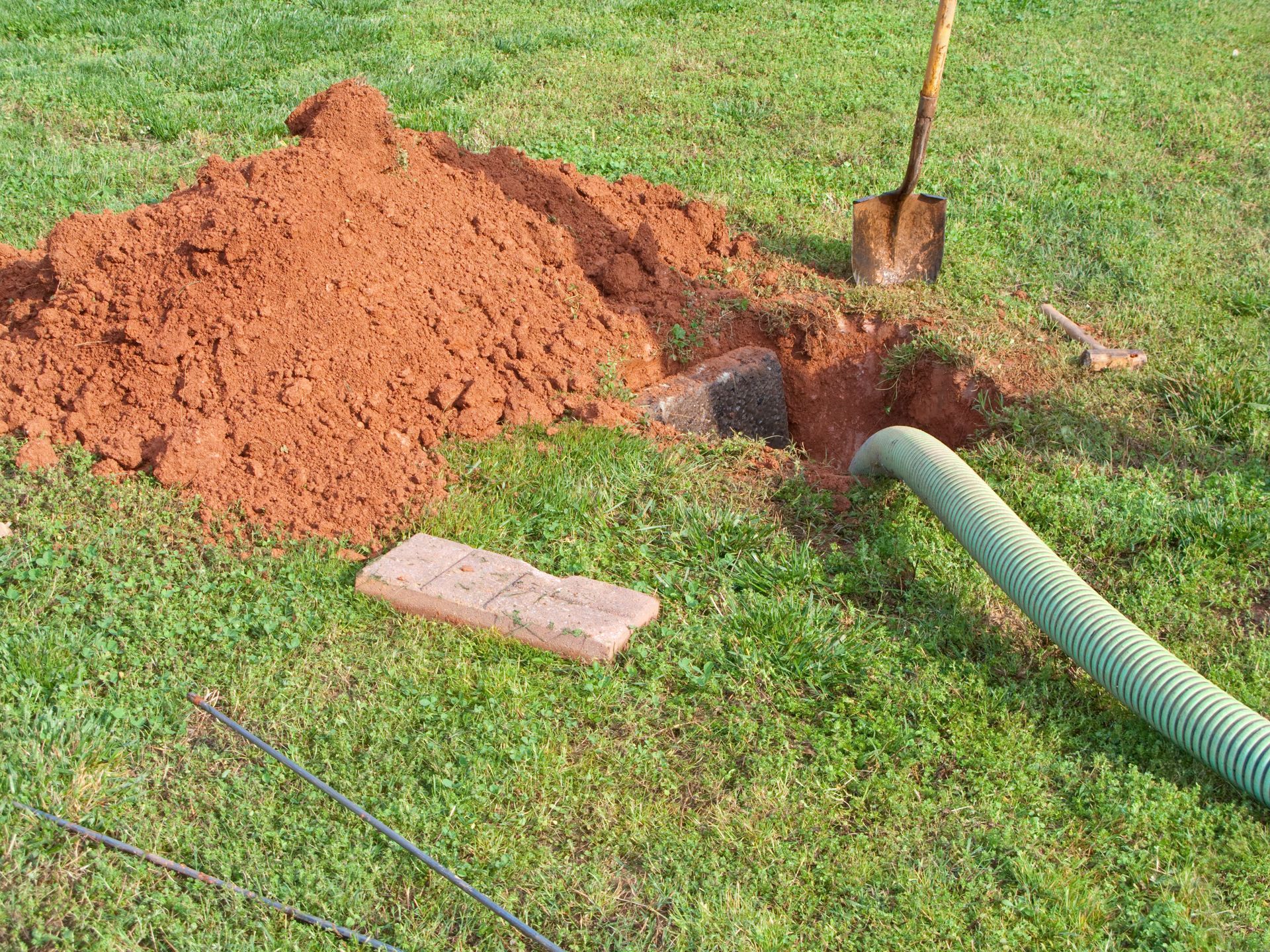 A green hose is coming out of a hole in the ground.