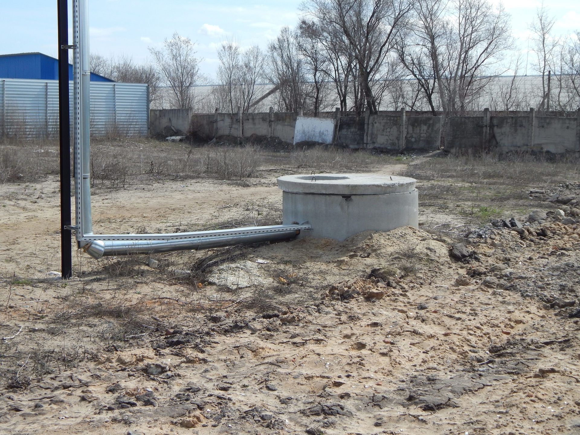 A concrete well in the middle of a dirt field