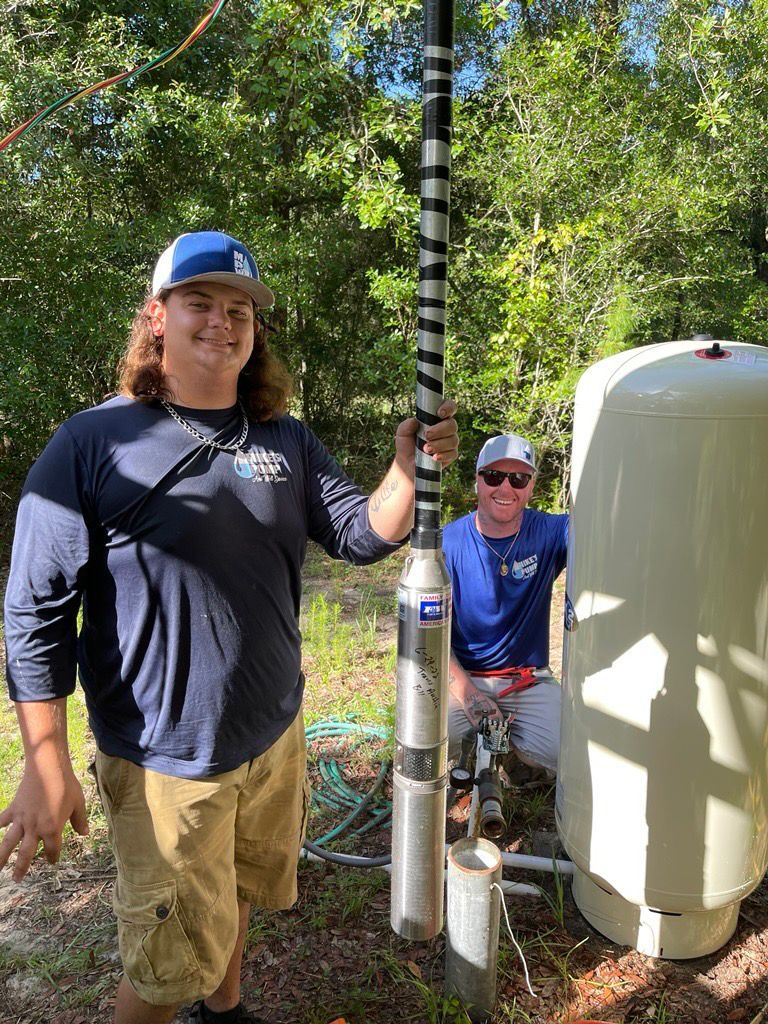 Two men are working on a water pump in the woods.