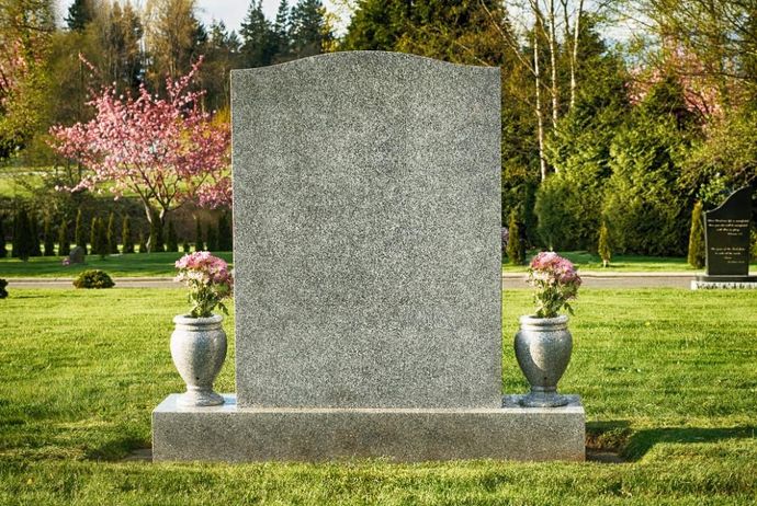 Blank headstone in a cemetery with two vases of flowers and green grass.